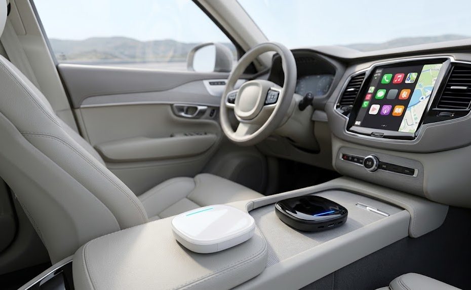 Wireless CarPlay adapter on a car centre console beside a screen showing app icons